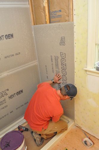 a man in an orange shirt is working on the walls of a bathroom under construction