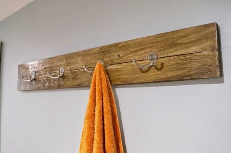 an orange towel is hanging on a wooden coat rack and hooks are attached to the wall