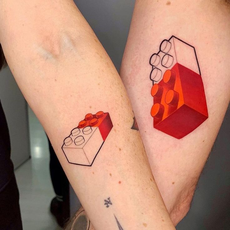 two people with matching tattoos on their arms, one is holding a lego block and the other has a red box