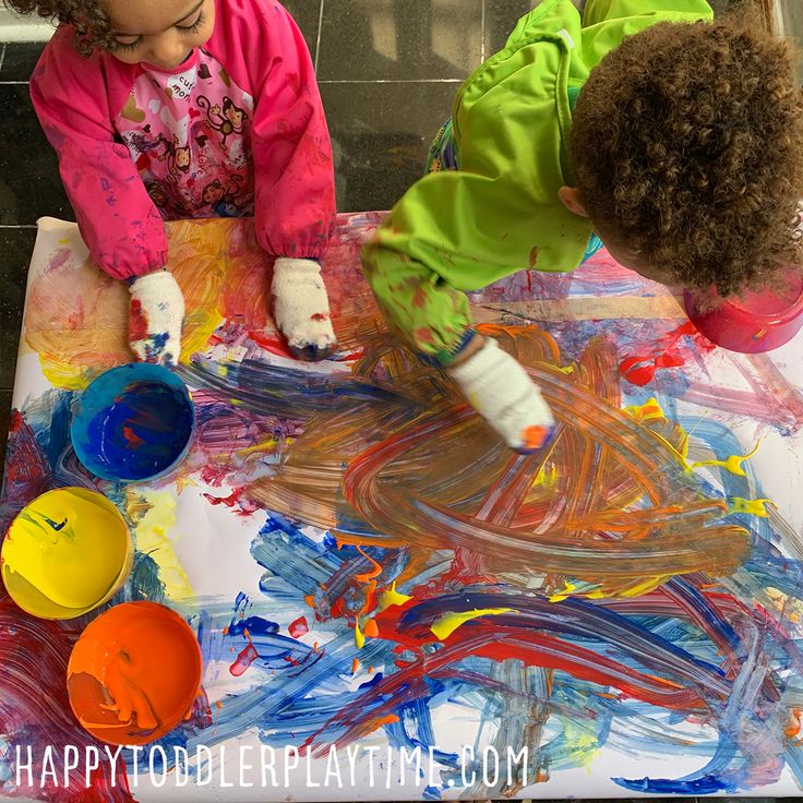 two children are playing with colorful paint on the floor