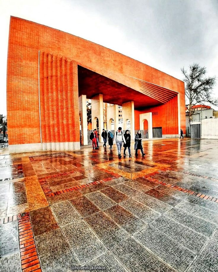 people are walking in front of an orange building with red and white tiles on the floor