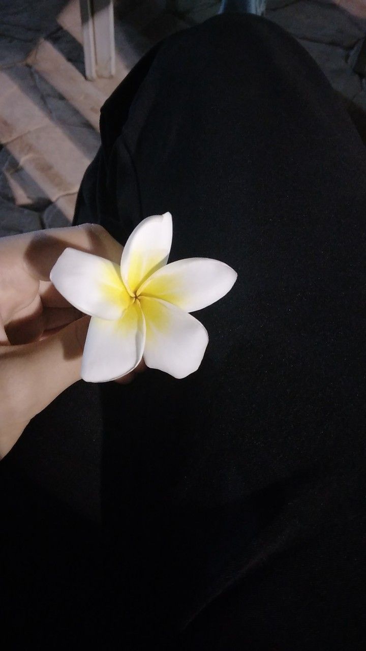 a white and yellow flower being held by someone's hand on a black shirt