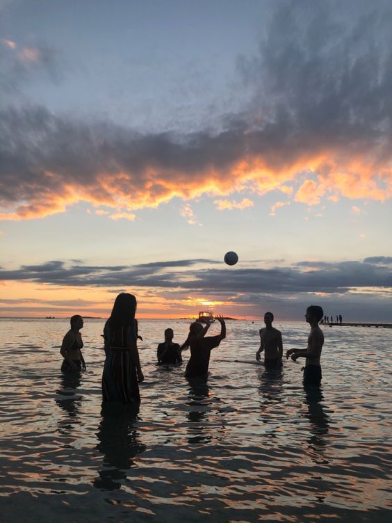 people are playing volleyball in the water at sunset