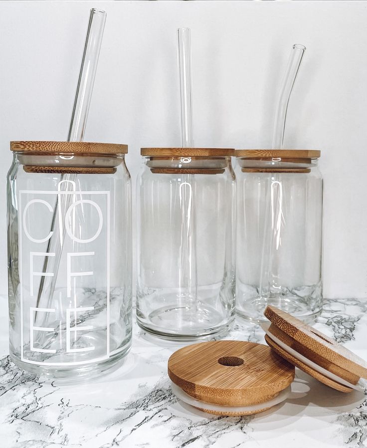 three glass jars with wooden lids and spoons on a marble countertop next to each other