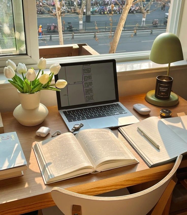 an open laptop computer sitting on top of a wooden desk next to a flower vase