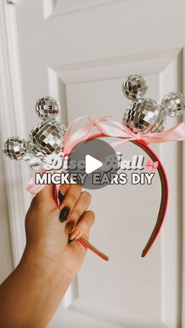 a woman is holding up a mickey ears headband with pink ribbon and crystal balls on it