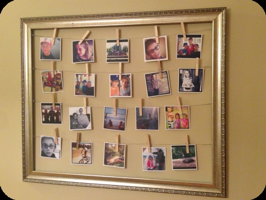 a photo frame with pictures pinned to clothes pins on a string attached to the wall