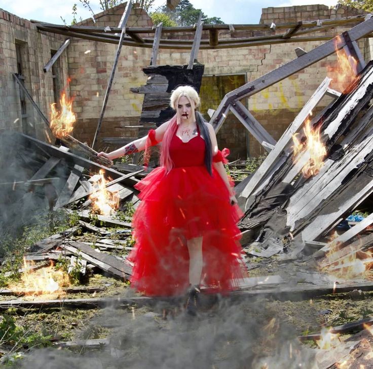 a woman in a red dress is walking through the rubble with fire coming from her legs