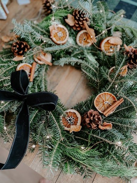 a christmas wreath with oranges and pine cones on the front, sitting on a wooden floor