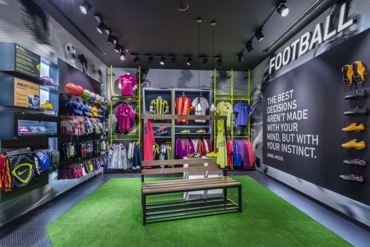 the inside of a sports shop with green carpeting and shelves filled with colorful shirts