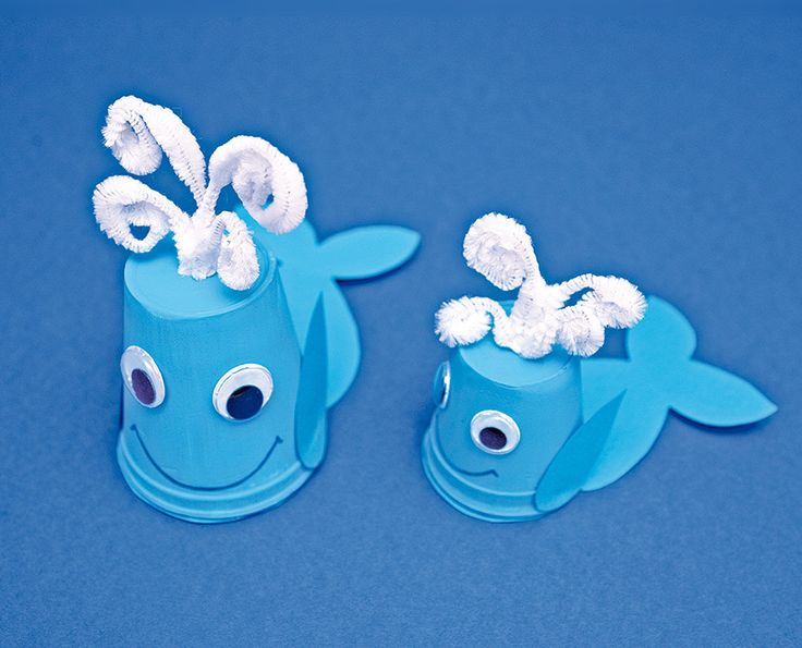 two blue paper cups with googly eyes and toothpicks on them sitting on a blue surface