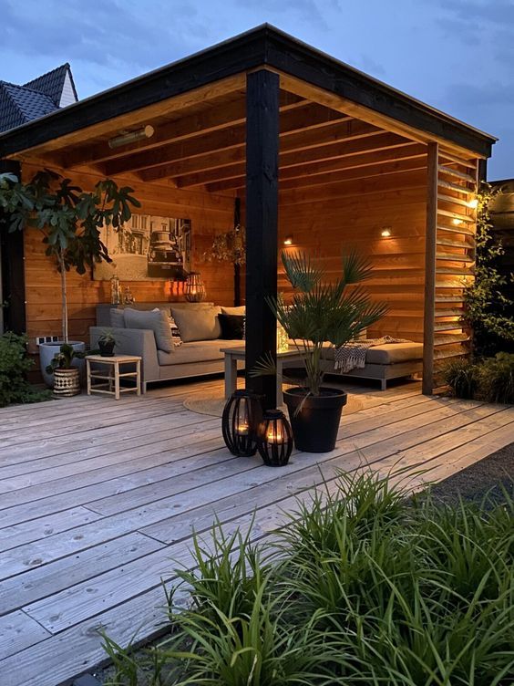 a wooden deck with potted plants and lights on it in front of a house