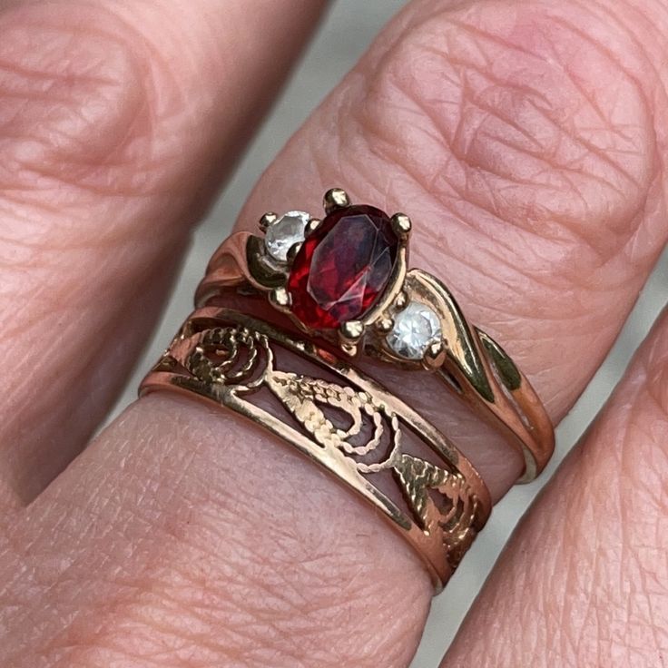 a close up of a person's hand with two rings on their fingers and one has a red stone in the middle