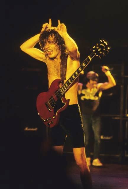 a man with long hair and no shirt holding a guitar in front of his head