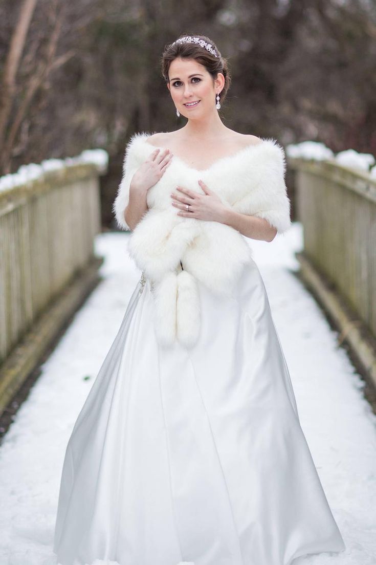 a woman in a white wedding dress and fur stoler on a bridge with snow