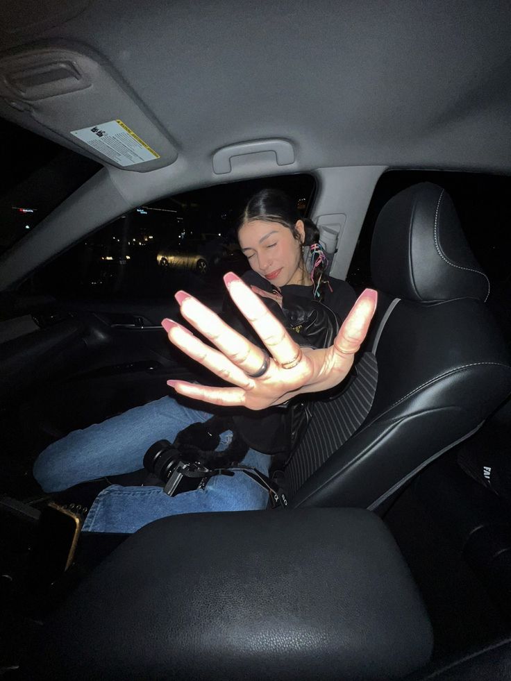 a woman sitting in the back seat of a car with her hands out to catch something