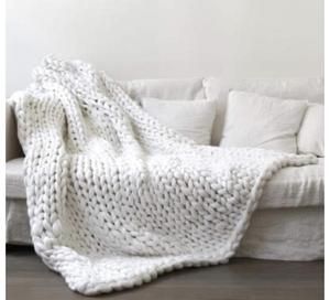 a white couch with a knitted blanket on it's back next to pillows