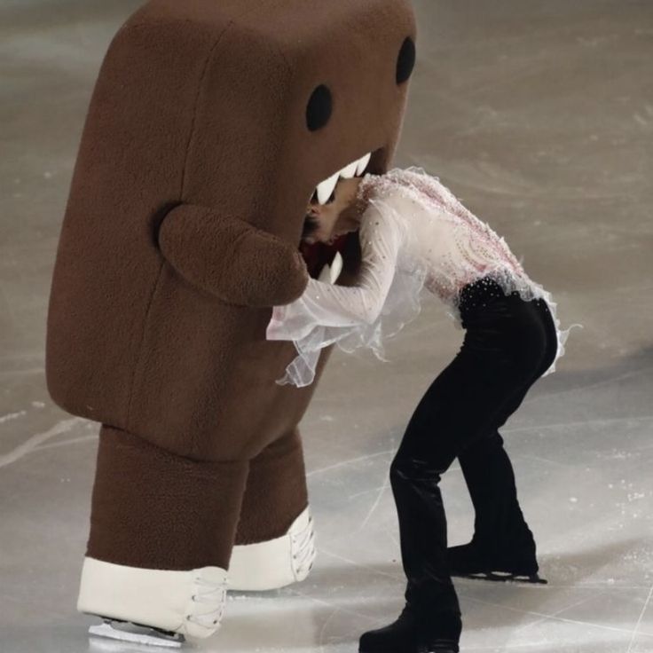 a person in a costume standing next to a giant stuffed animal on a ice rink