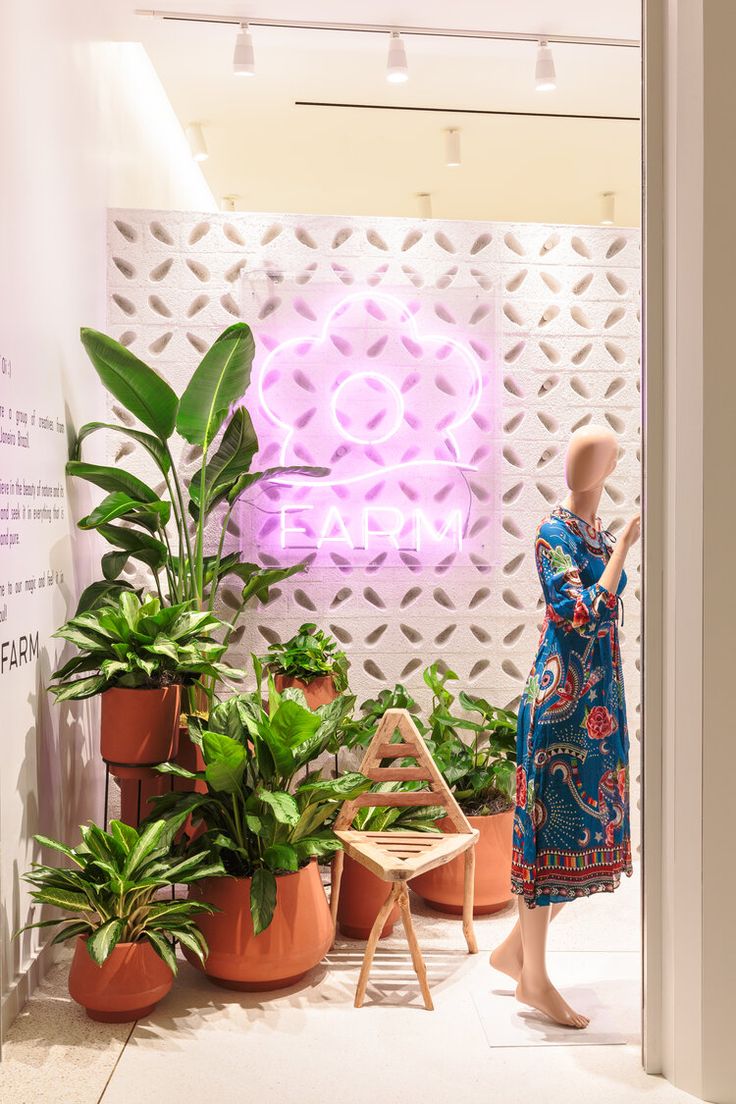 a mannequin is standing in front of potted plants and a neon sign