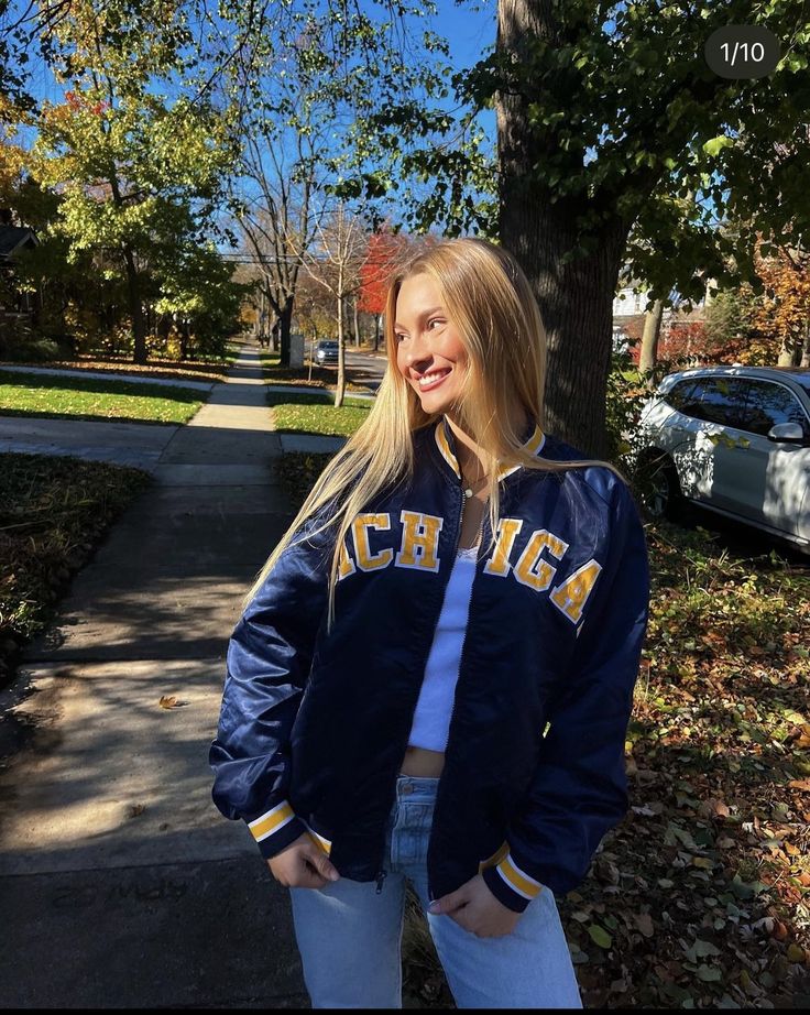 a girl standing on the sidewalk in front of a tree wearing a jacket that says michigan