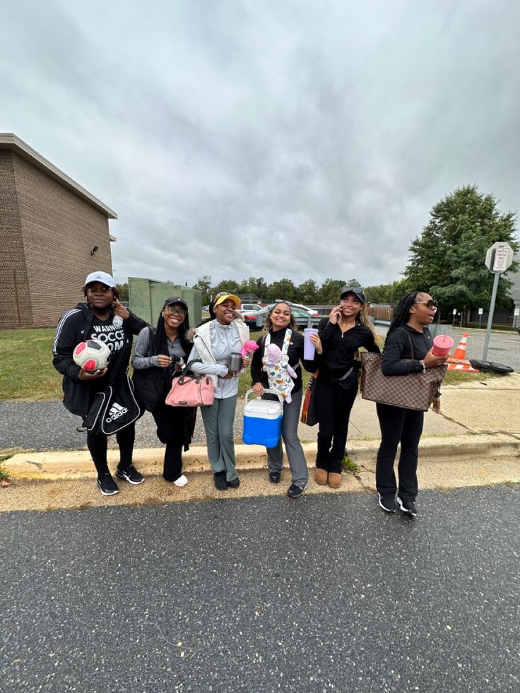 four people standing on the side of a road holding pink and blue bags with hearts