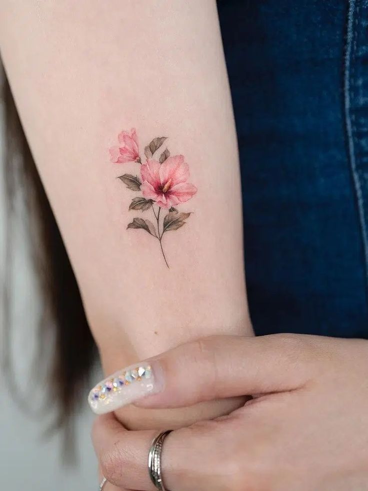 a woman's arm with a pink flower tattoo on the left side of her arm