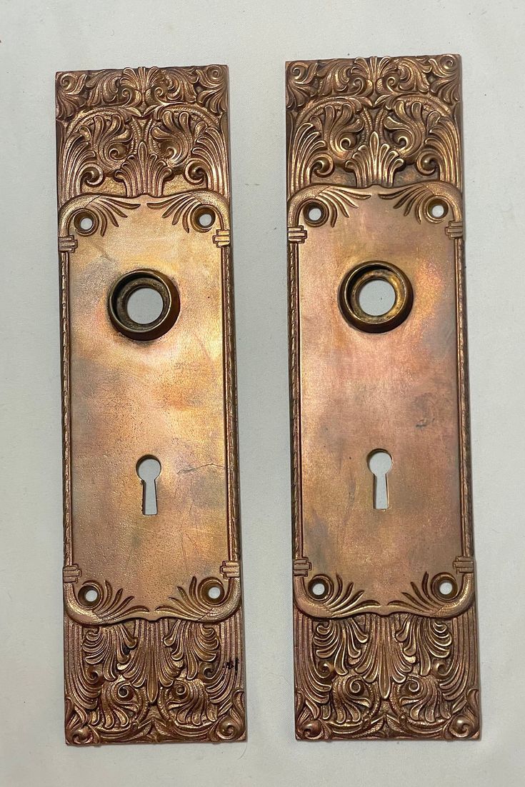 two antique brass door handles with ornate designs and keyholes on each one side