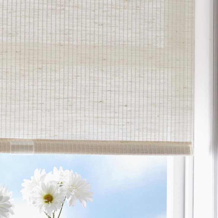 two white daisies in a vase on a window sill with the blinds closed