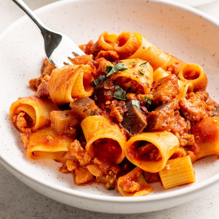 two white bowls filled with pasta and meat on top of a table next to a fork