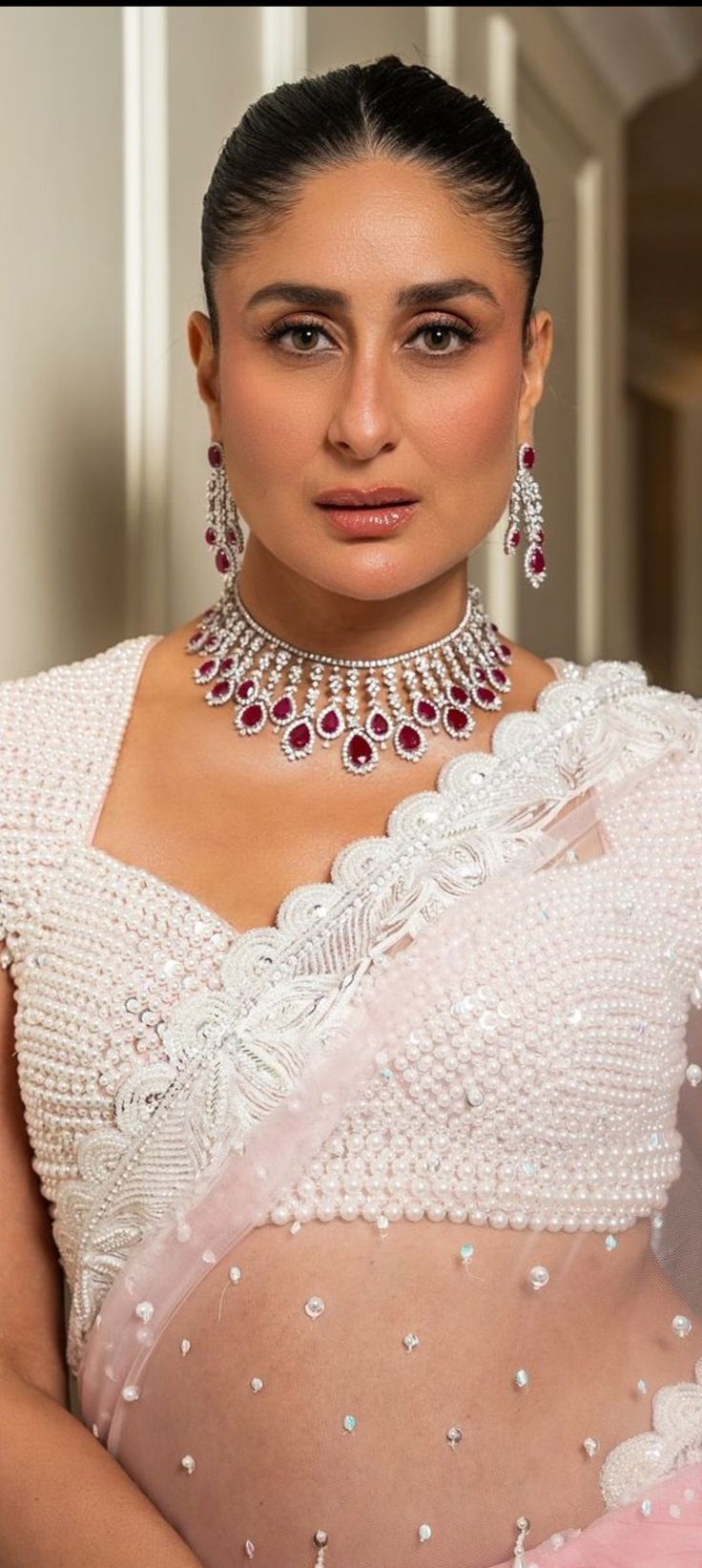 a woman in a white dress wearing a necklace and earrings with red stones on it