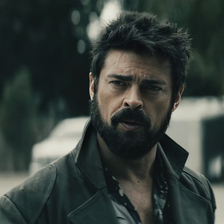 a man with a beard wearing a leather jacket and looking at the camera while standing outside