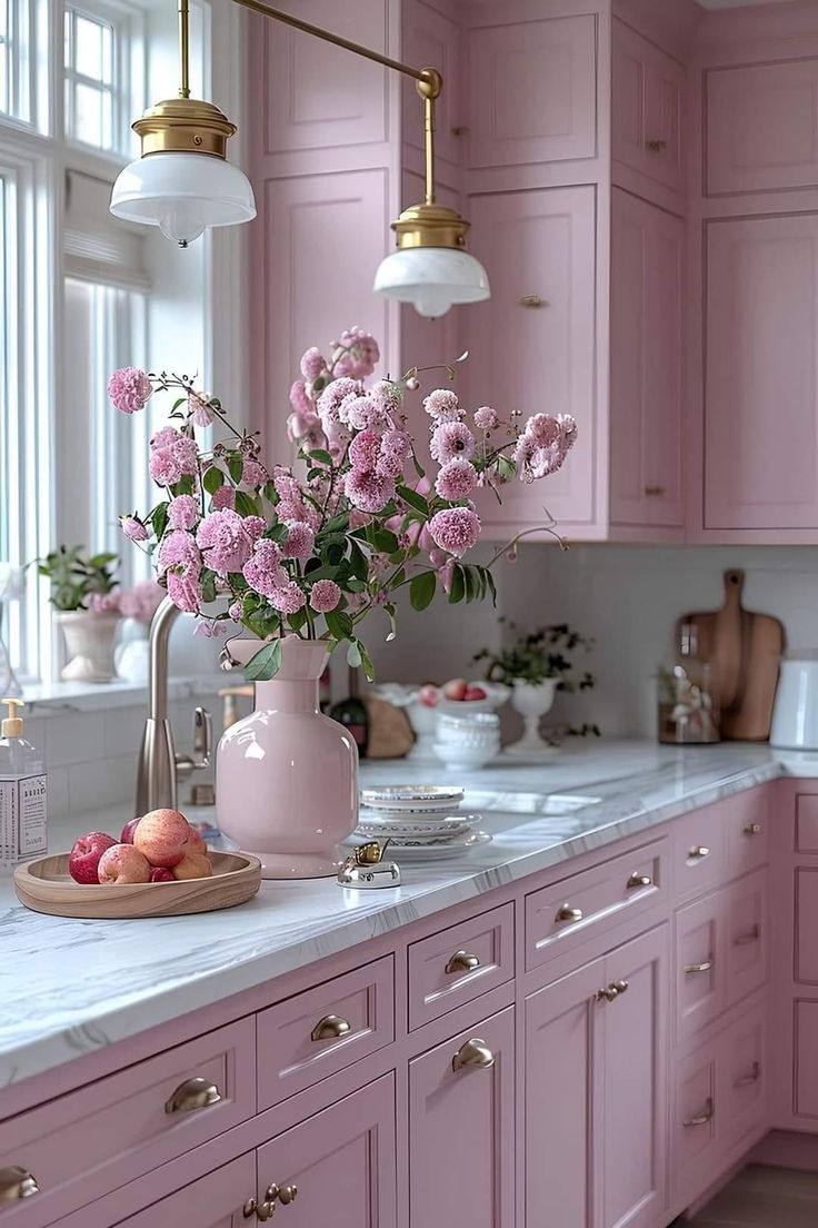 a kitchen with pink cabinets and marble counter tops, flowers in a vase on the island