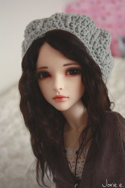 a close up of a doll wearing a knitted hat on top of a bed