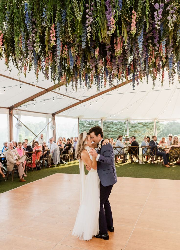 a bride and groom share their first dance under the tented ceiling with flowers hanging from it