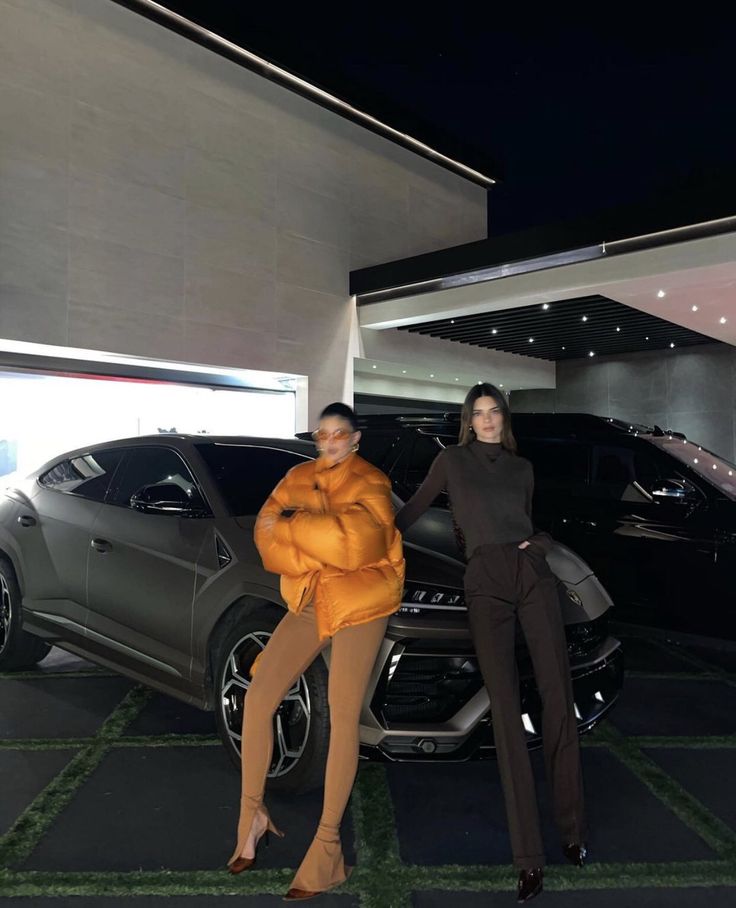 two women standing next to each other in front of cars