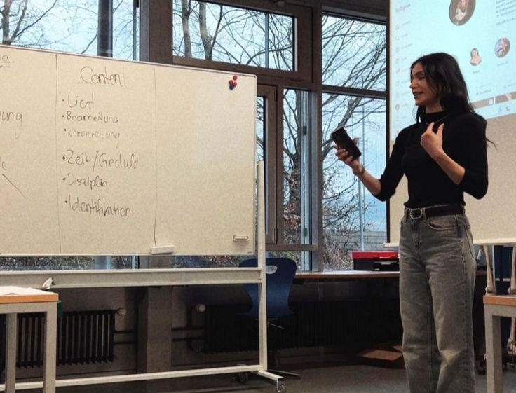 a woman standing in front of a whiteboard with writing on it and holding a cell phone