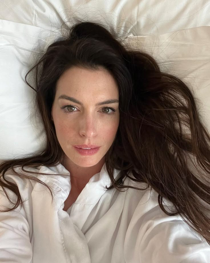 a woman laying on top of a white bed with her hair blowing in the wind