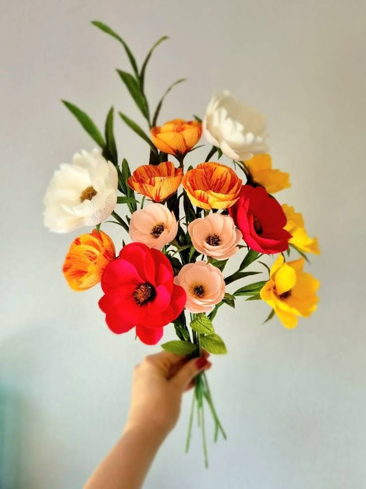 a person holding a bouquet of flowers in their hand with white, yellow and red flowers