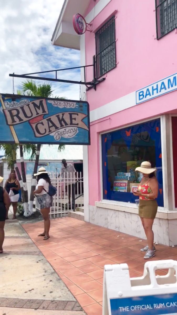 some people are walking down the sidewalk in front of a pink and white building with a sign that says rum cake