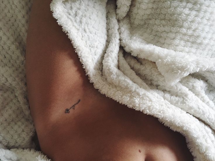 a woman with a small tattoo on her stomach under a white blanket covered in blankets