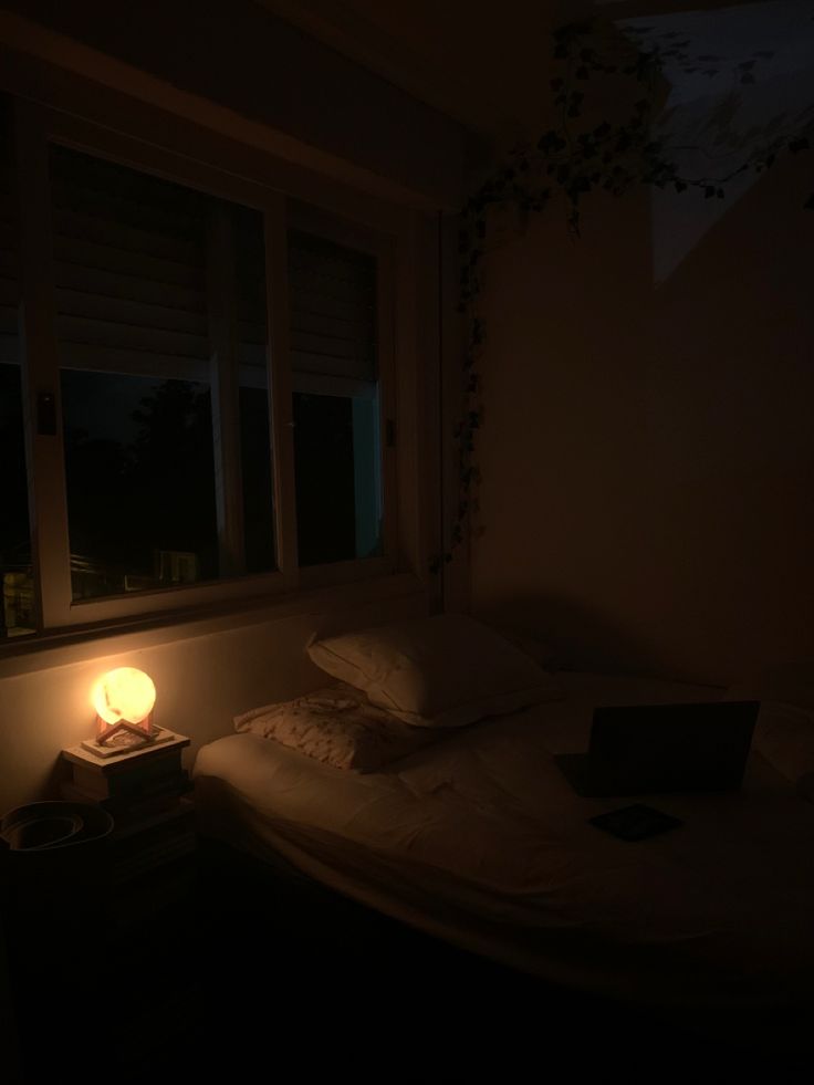 a dimly lit bedroom with a laptop on the bed and a window in the background