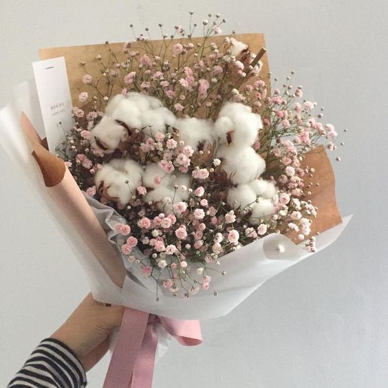 a person holding a bouquet of cotton and flowers