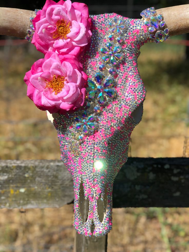 a cow skull with pink flowers on it's head sitting in front of a fence