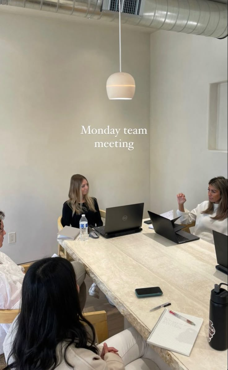 four people sitting at a table with laptops and papers in front of them that say monday team meeting