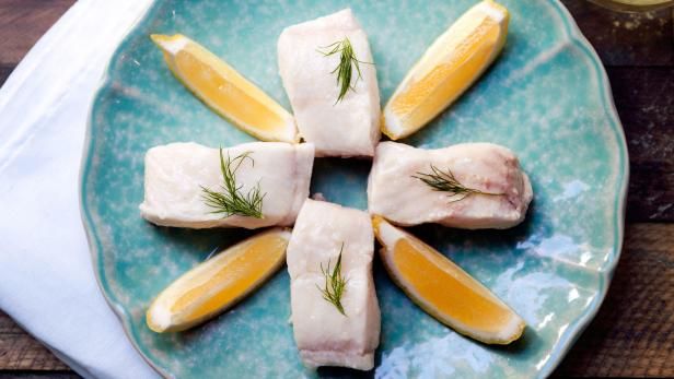 four pieces of fish on a plate with lemons and dill garnish