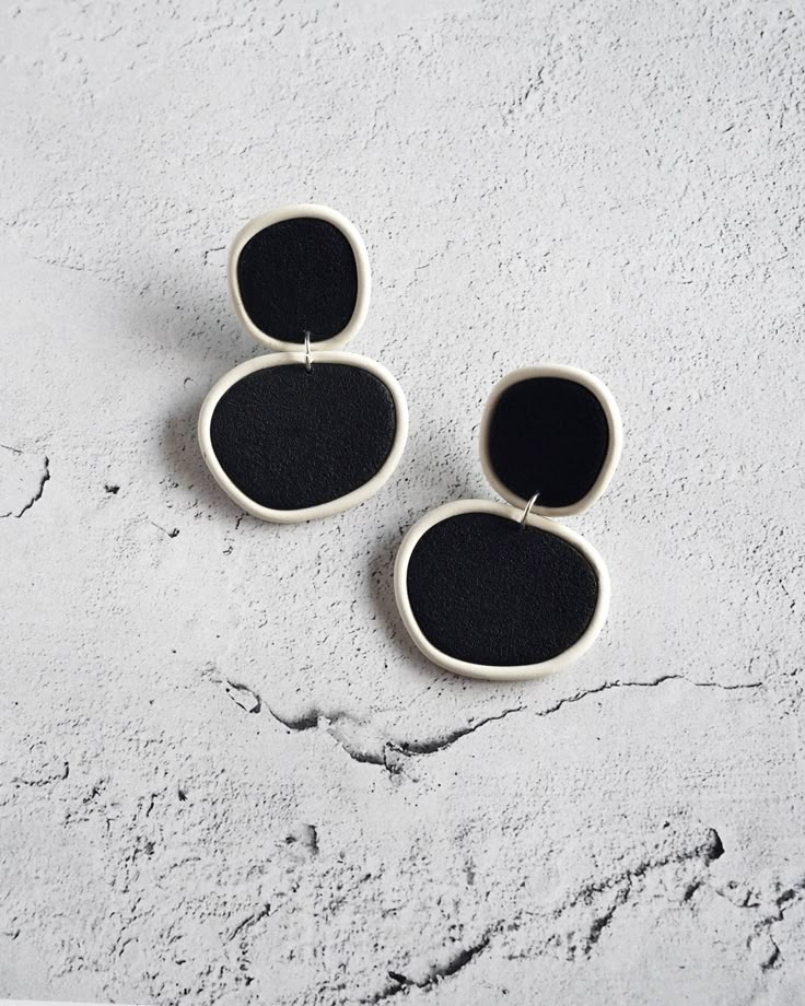 two black and white oval shaped earrings sitting on top of a cement surface with one earring in the shape of an oval