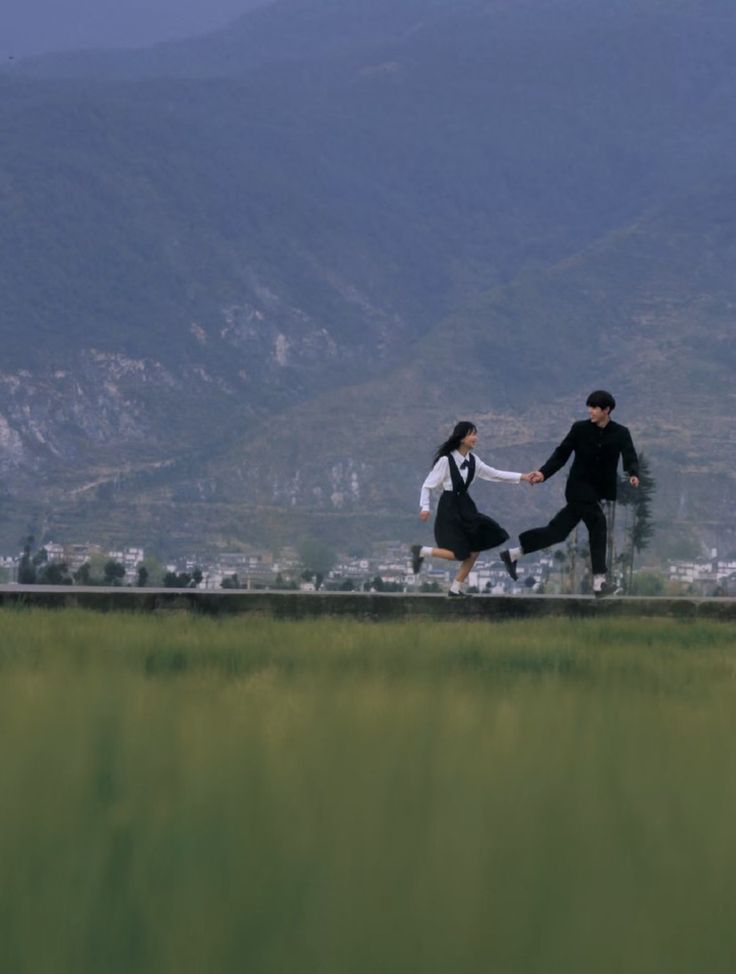 two people dressed in black and white are running across the grass with mountains in the background