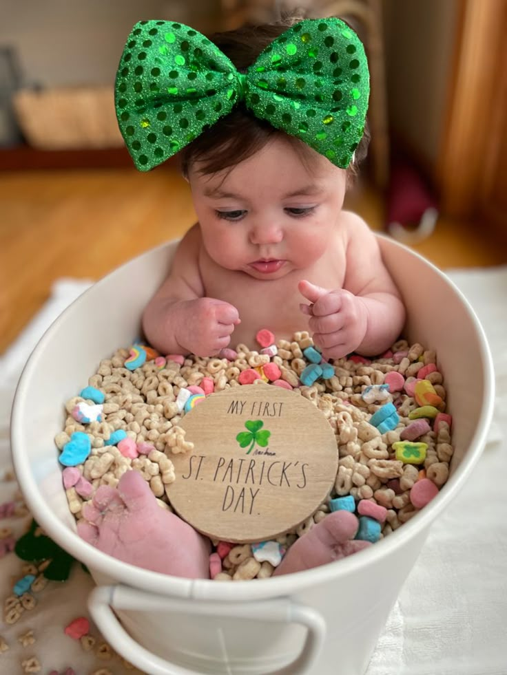 a baby in a white bowl with a green bow on it's head and its name is st patricks day