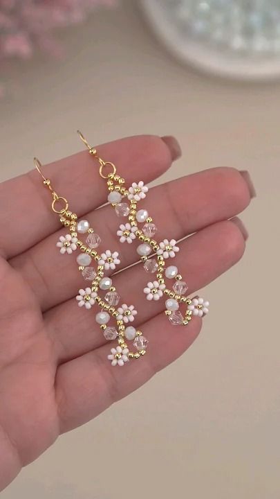 a person is holding some white flowers and pearls on their earring wires, while wearing a pair of gold - plated earrings