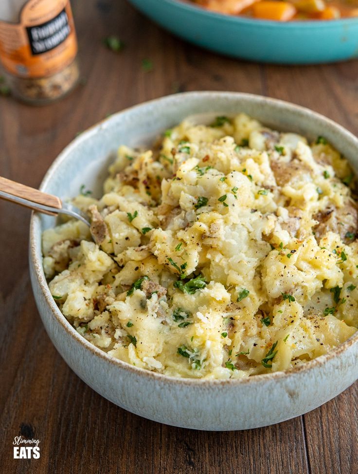 a bowl filled with mashed potatoes on top of a wooden table next to a jar of mustard